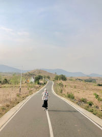 Rear view of man walking on road against sky