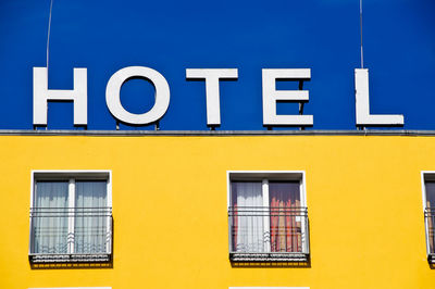 Low angle view of hotel text on yellow building against blue sky