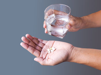 Close-up of hand holding glass over water against gray background