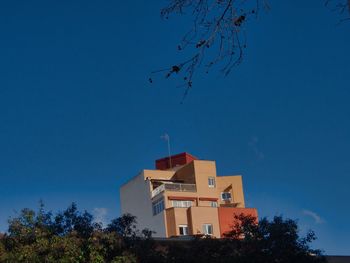 Low angle view of building and trees against clear blue sky