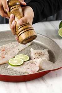 Woman hand grinding pepper onto fillet fish on a pan using wooden pepper mill