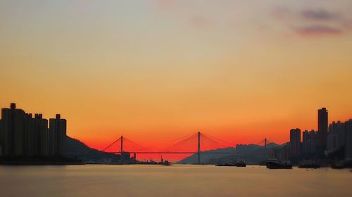 Silhouette of suspension bridge over river during sunset