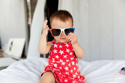 Cute baby girl wearing sunglasses while sitting on bed at home