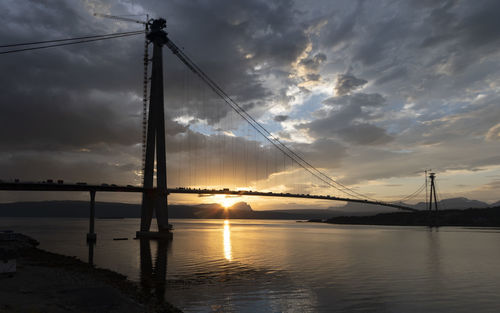 Silhouette bridge over sea against sky during sunset