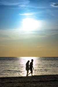 Silhouette people on beach against sky during sunset