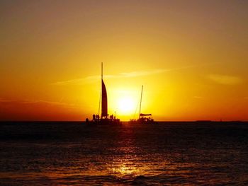 Silhouette sailboat sailing on sea against orange sky