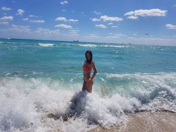 Young woman in bikini standing in wave at seashore