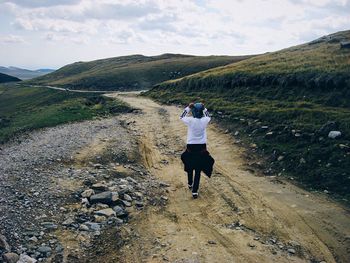 Rear view of woman walking on road at mountain against sky