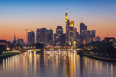 Illuminated buildings by river against sky in city