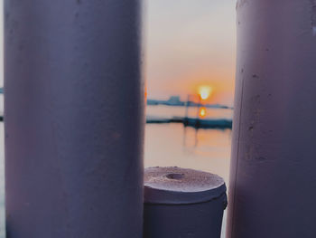 Close-up of metal railing against sea during sunset