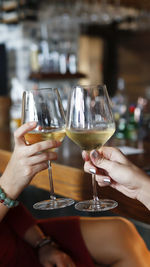 Two girls cheers with glass of cold white wine in the bar. close up of two wine glasses toasting.