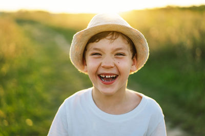 Portrait of a smiling little boy in a white t-shirt and hat playing outdoors on the field at sunset