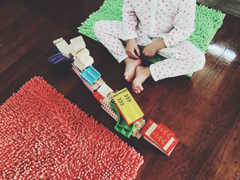 Low section of person sitting in front of stacked toys on floorboard