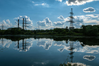 Reflection of a power line, two tall pipes and clouds in the water of the uvod river on a summer day