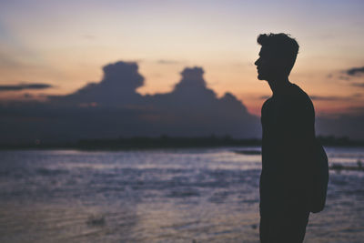 Silhouette man standing in front of sea during sunset