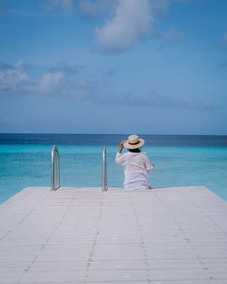 Rear view of woman sitting by swimming pool against sky