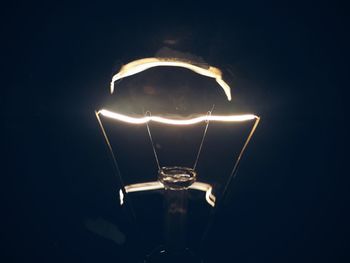 Close-up of illuminated light bulb against black background