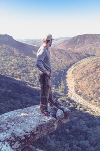 Man standing on rock formation while looking at mountains