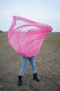 Woman playing with pink tulle net on dirt field
