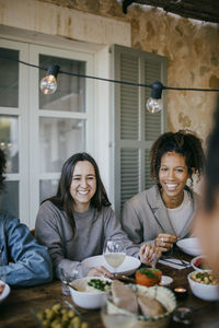 Cheerful young female friends sitting at dining table in patio for dinner party