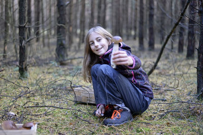 Portrait of smiling cute girl collecting edible mushroom in forest