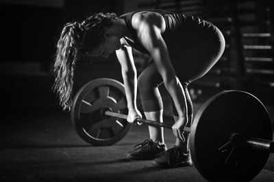 Woman lifting barbell in darkroom