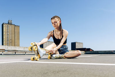 Girl tying up her roller skates, urban background