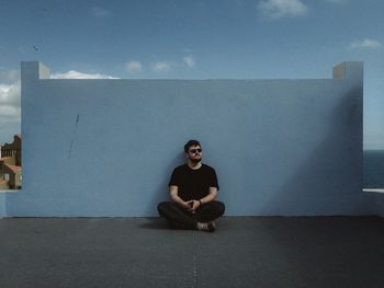 Portrait of young man sitting against wall