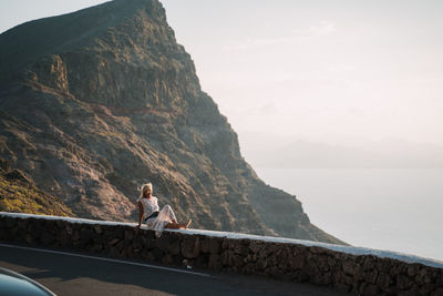 Full length of woman sitting on retaining wall against valley