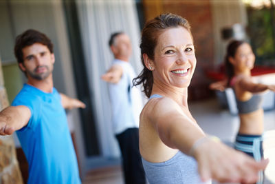 Portrait of smiling woman doing stretching exercise with friends at studio