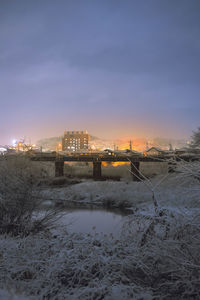 Frozen river amidst buildings against sky during sunset