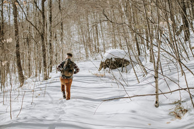 Man wearing pack walks and hikes through snow covered trees and woods