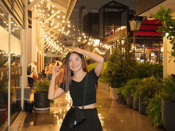 Portrait of young woman standing against illuminated city at night