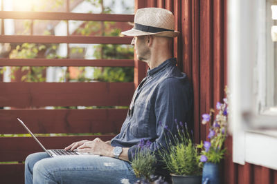 Side view of man sitting with laptop in back yard