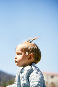 Side view of cute baby girl sitting against sky