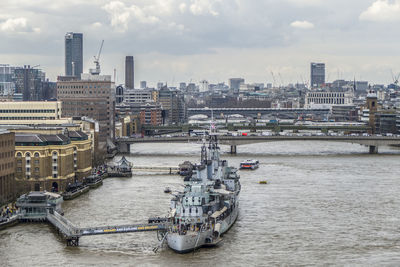 Nautical vessel on river by buildings in city against sky