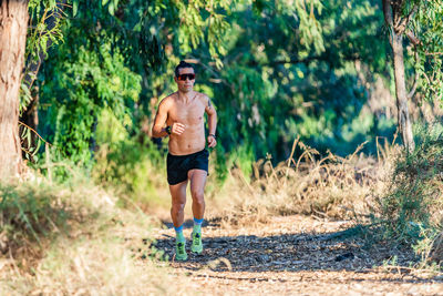 Full length of shirtless man running in forest