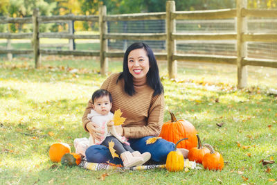 Portrait of mother with cute daughter sitting by pumpkins on land during autumn