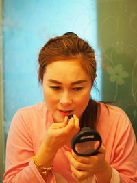 Close-up of woman applying lipstick looking at hand mirror