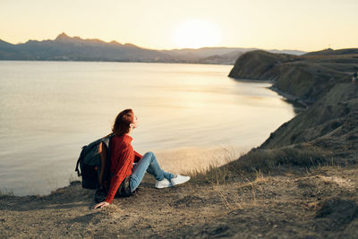 Man sitting on rock at beach against sky during sunset