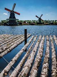 Tree trunks floating on the water in front of windmills and the sky 