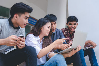Smiling university students using laptop while sitting indoors