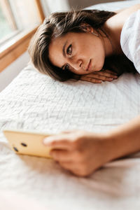 Side view of young woman using mobile phone while lying on bed at home