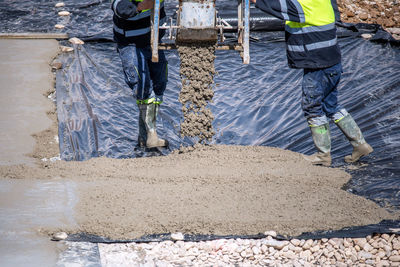 Two construction workers at work pouring a mixture on a floor with a plastic sheet.