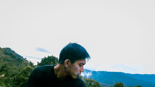 Portrait of young man looking at mountains against sky