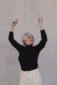 Mature woman looking away while dancing in front of wall