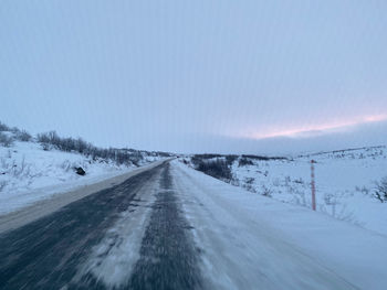 Road amidst snowcapped landscape against sky during winter