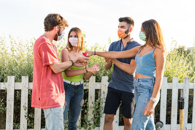 Friends using hand sanitizer while standing outdoors