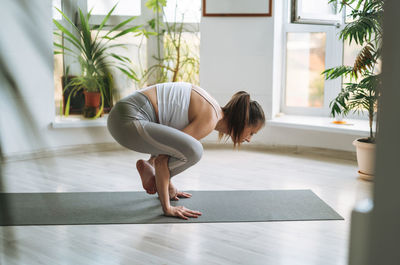 Young fit woman practice yoga doing asana in light yoga studio with green house plants