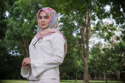 Portrait of beautiful young woman in hijab standing against trees